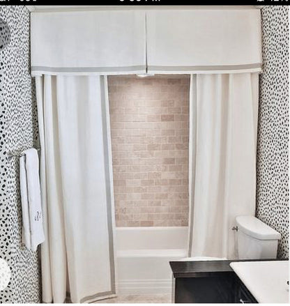 Custom white shower curtain with grey trim and matching pleated valance in a white-tiled bathroom