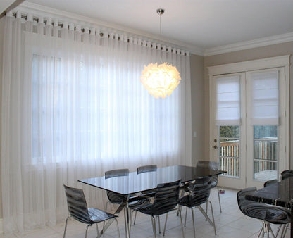 Dining room with white Lucky sheer grommet panels behind a glass table
