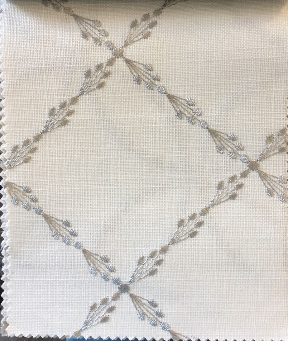 Fabric close-up showing silver embroidered sprigs on white linen weave