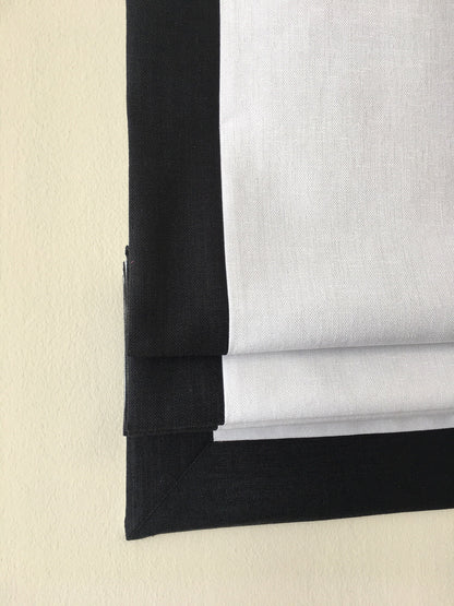 Relaxed fold Roman shade in white faux linen with contrast black trim