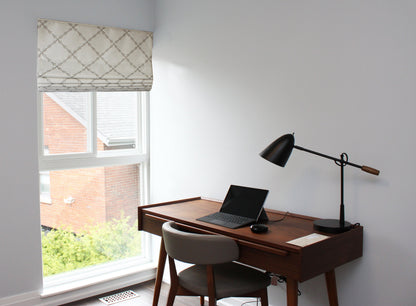 Home office with wooden desk, laptop and lamp beneath the Ryder Silver Roman shade