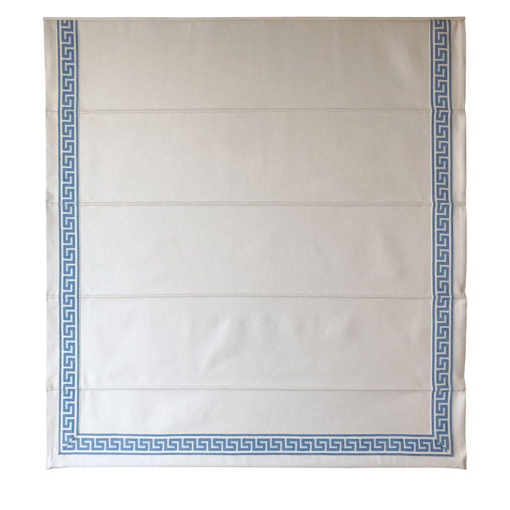 Close view of the blue Greek key trim along the hem of a white Roman shade