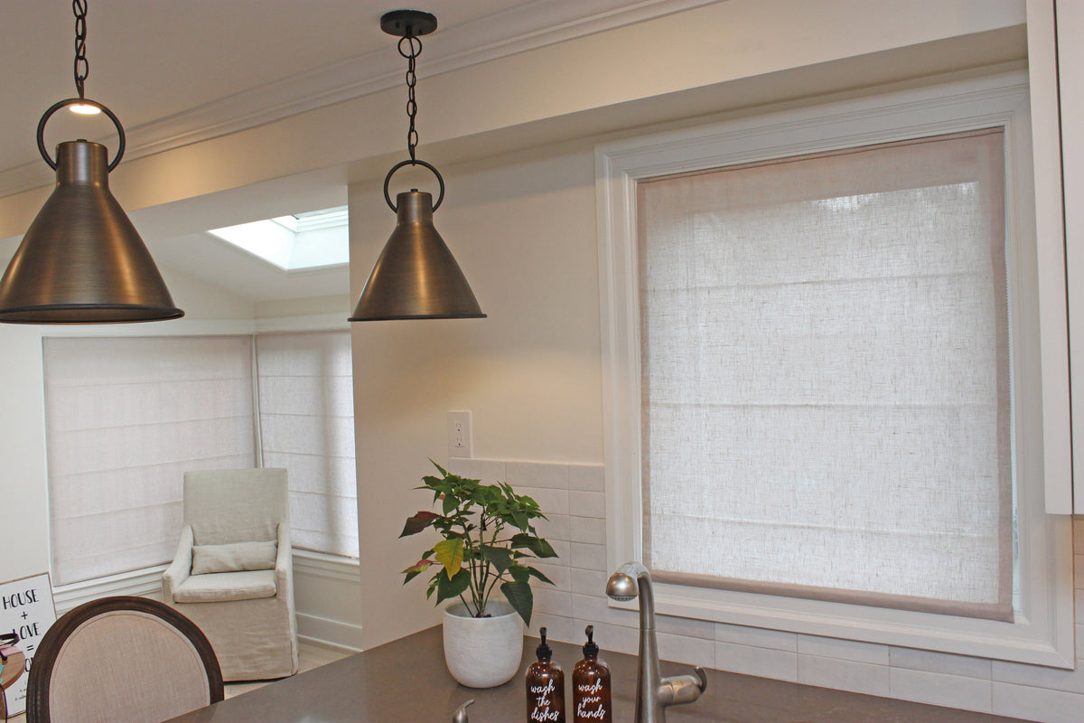 Linen Roman shades beside a pendant light and a plant in a bright skylit room