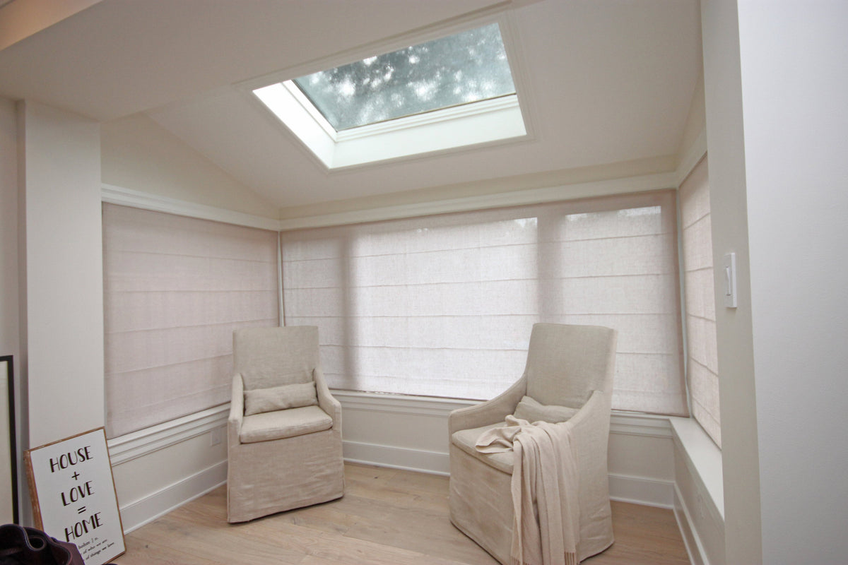 Relaxed linen Roman shades in a skylit sitting room with a slipcovered armchair
