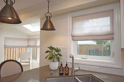 Custom Zoe Italian linen relaxed Roman shade over a kitchen sink, soft folds, pendant lights and a plant