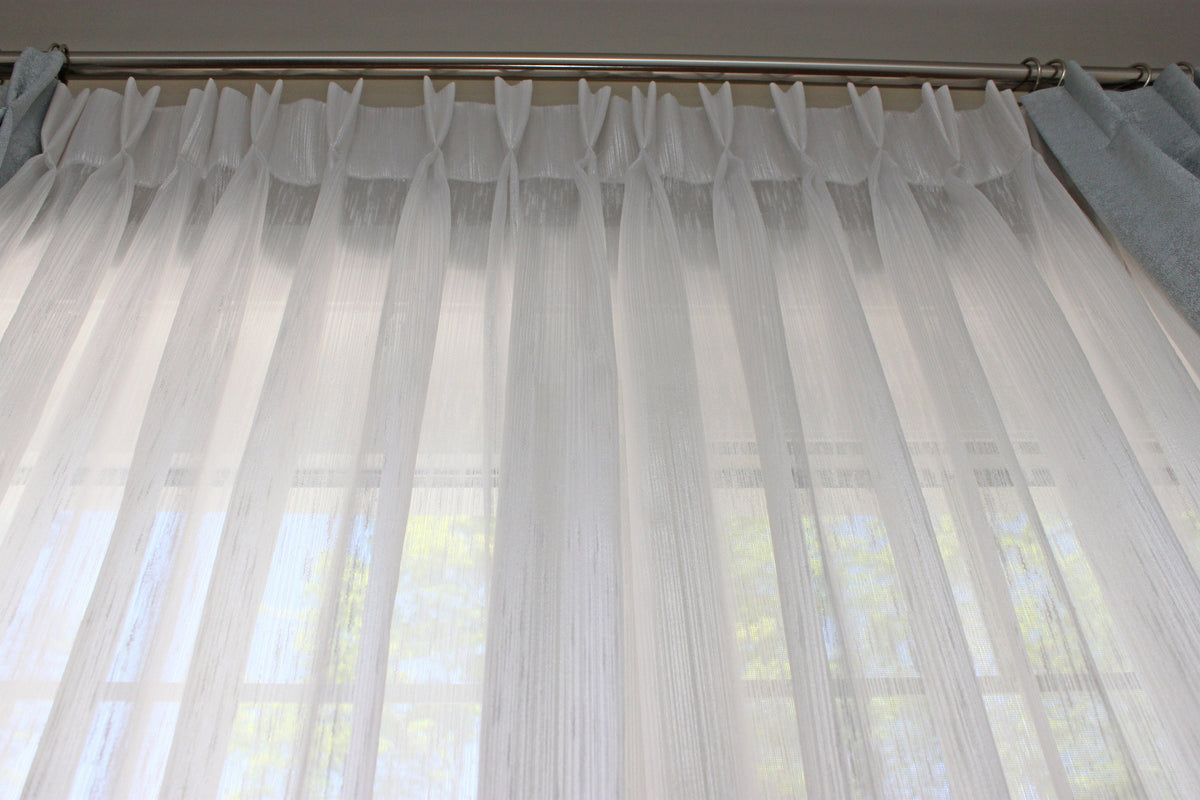Lugano pinch pleat sheer drapery panel hanging at a window