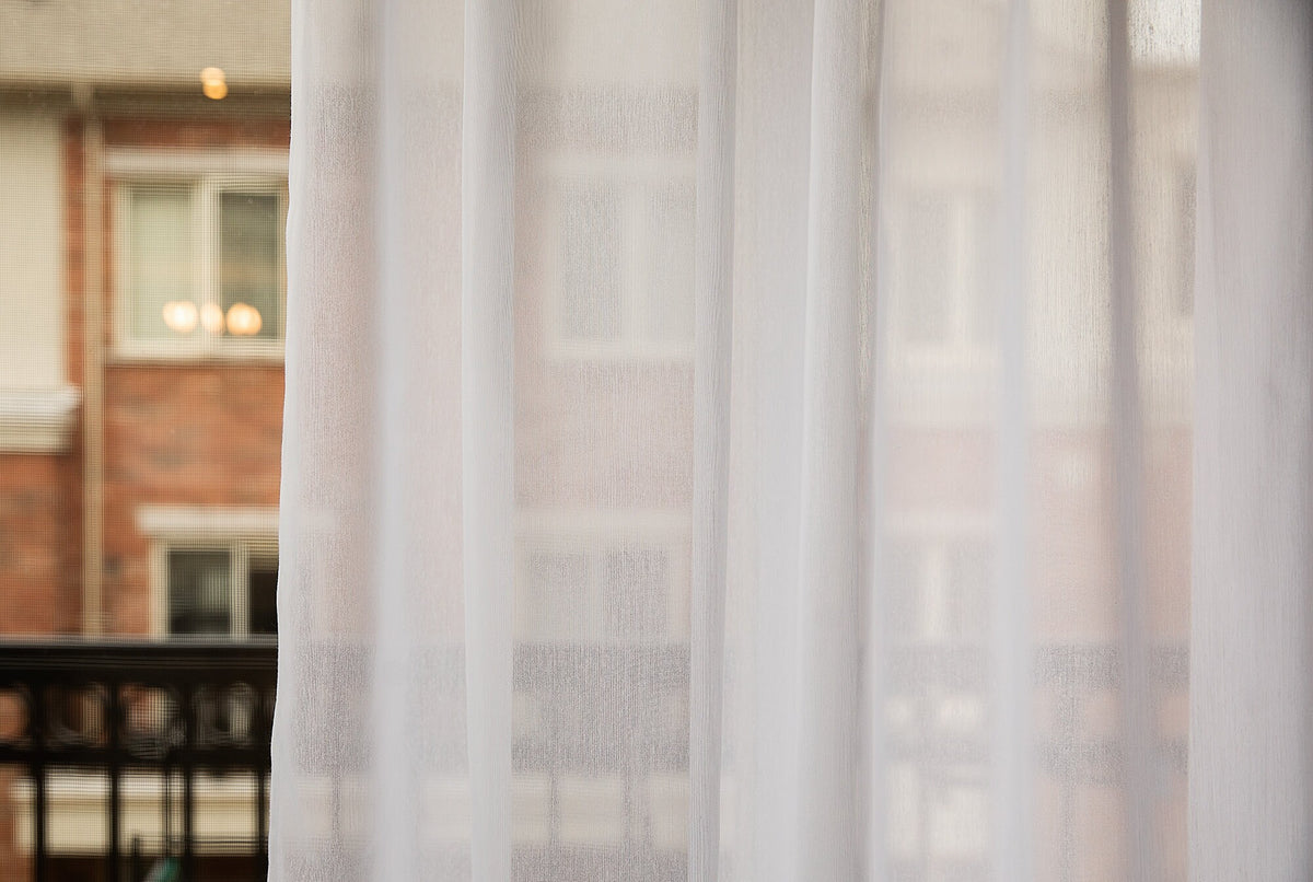 Dallas sheer panel at a window, brick building softly visible through the fabric