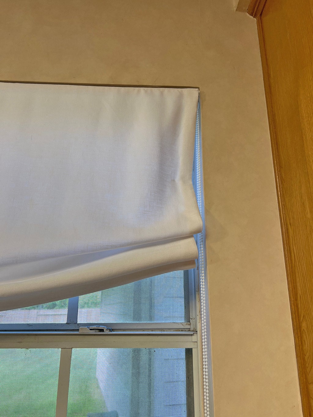 Customer photo: top corner detail of a white Roman shade inside mounted in the window recess