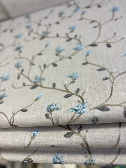 Close-up of Beatrix fabric — blue flowers and brown stems on a natural linen-look ground