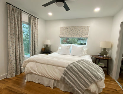 Bedroom with Beatrix floral Roman shade on one window and matching drapery panels on the other