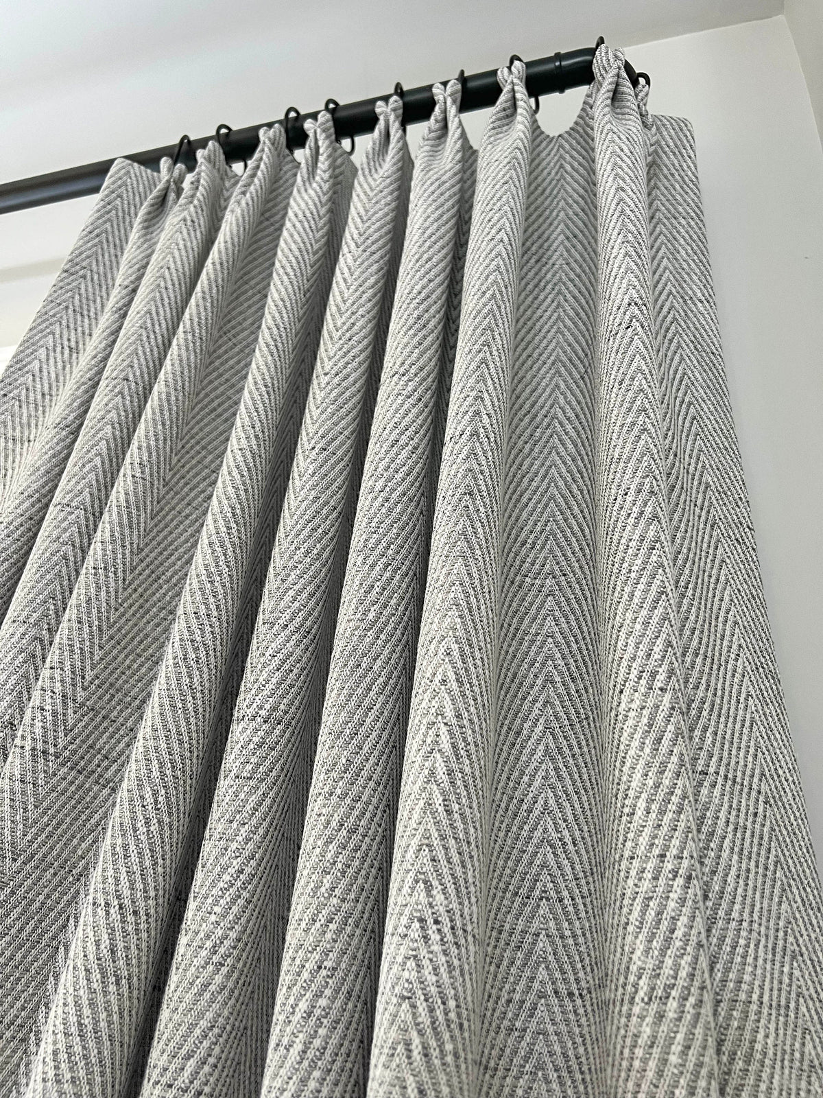 Corrie French pleat lined drapery panels in grey and white herringbone on a black rod