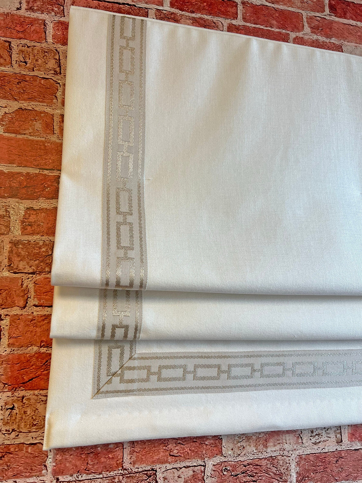 Relaxed linen Roman shade with black and white Greek key trim hanging in a bright living room window