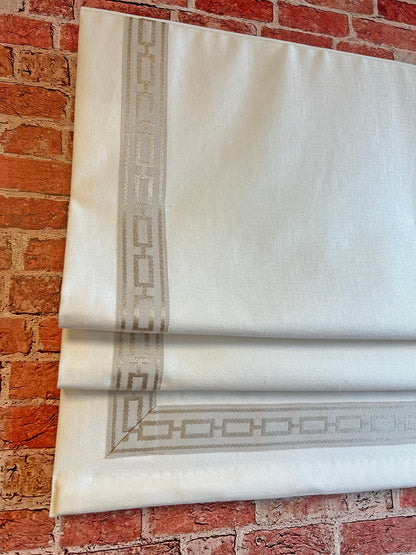 Relaxed linen Roman shade with black and white Greek key trim hanging in a bright living room window