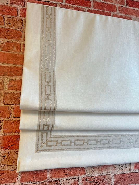 Relaxed linen Roman shade with black and white Greek key trim hanging in a bright living room window