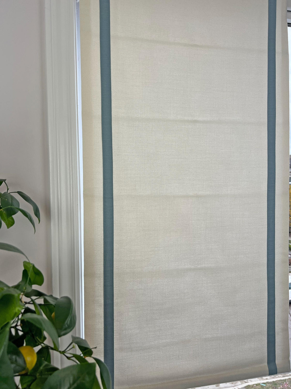Relaxed Roman shade with contrast border shown raised, folds falling softly