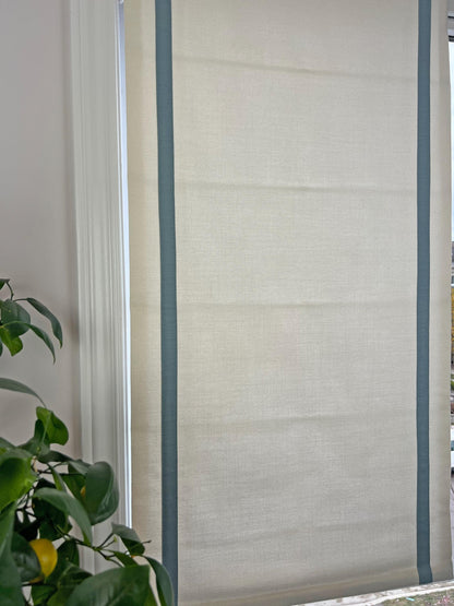 Relaxed Roman shade with contrast border shown raised, folds falling softly