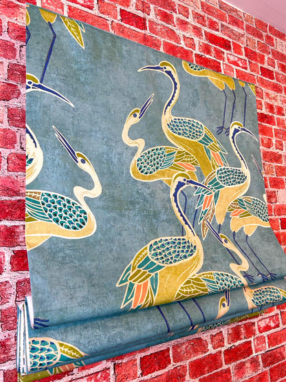 Deco Cranes fabric close-up — cranes in pool blue with olive and coral, on brick