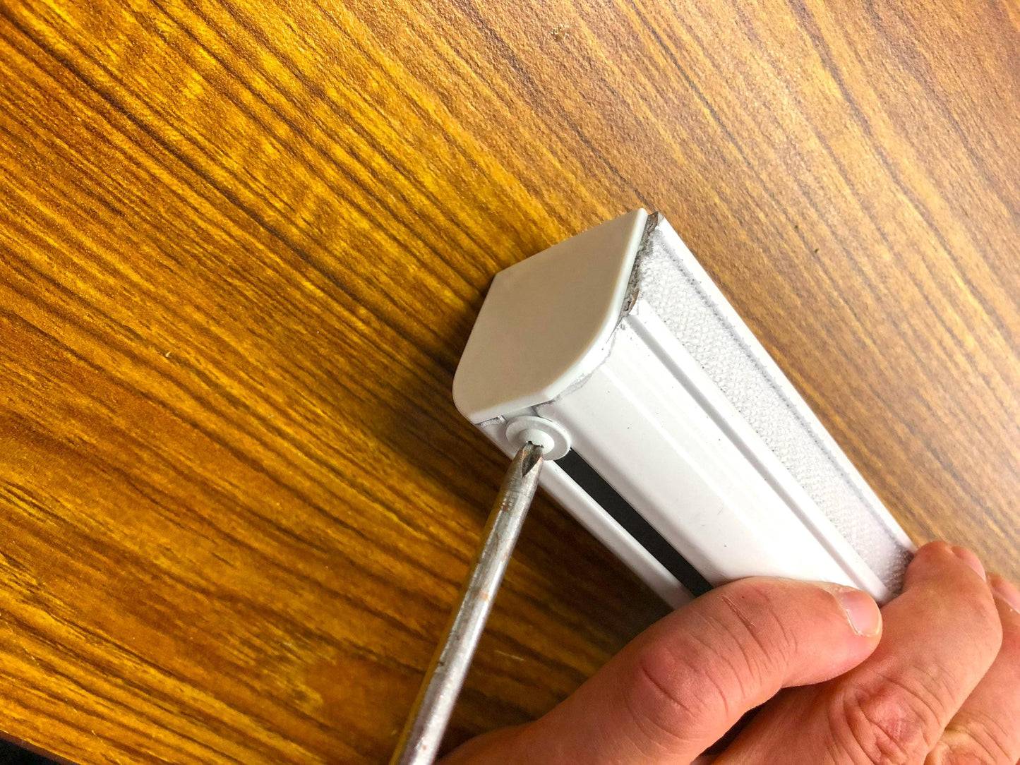 Close-up of chain clutch mechanism and end cap on white Roman shade track, replacement Roman blind hardware