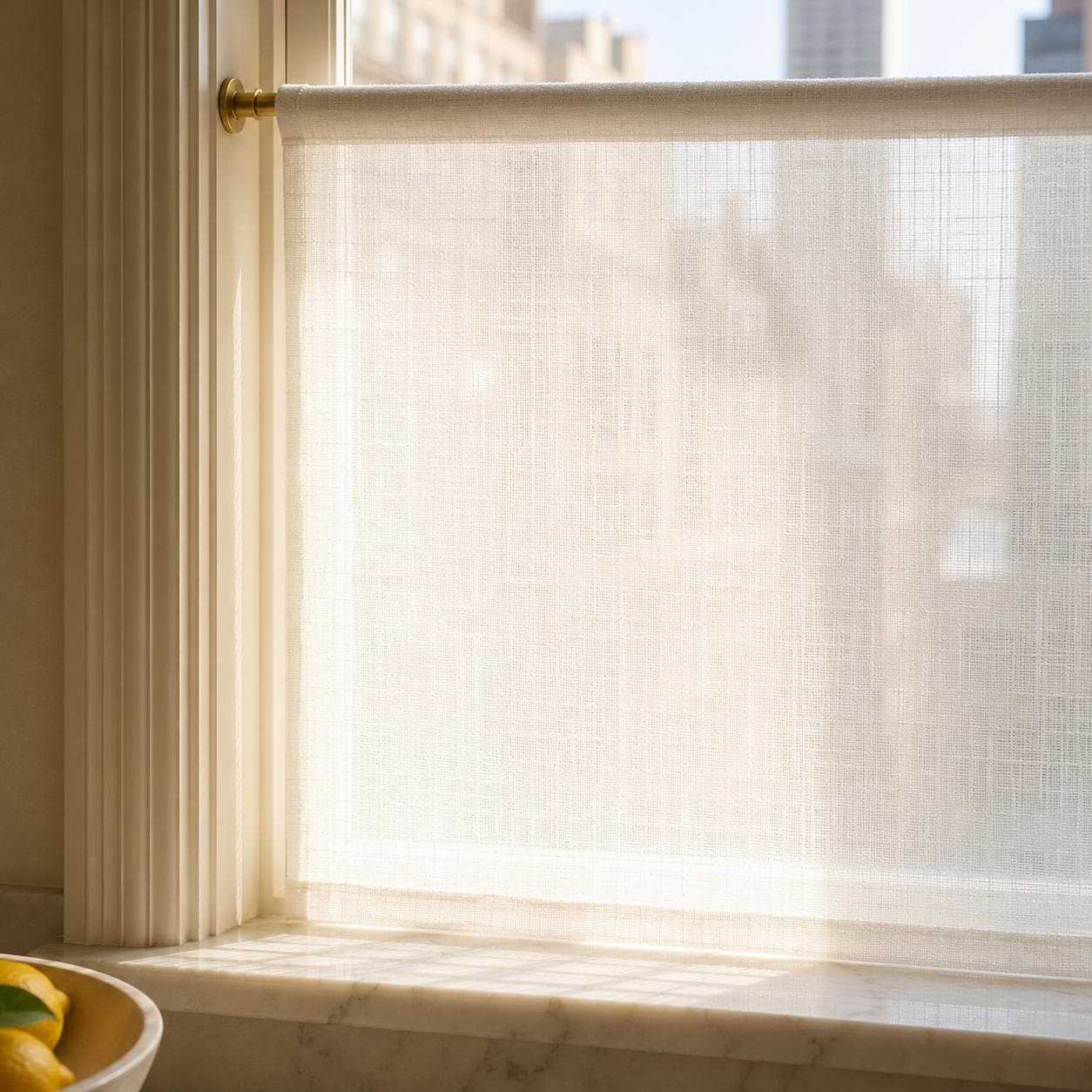 Sunlight glowing through the open weave of a sheer linen cafe curtain on a brass rod, softening the city view while keeping the room bright