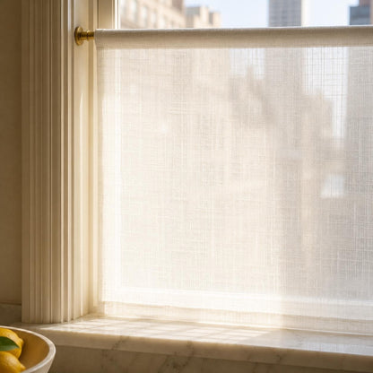 Sunlight glowing through the open weave of a sheer linen cafe curtain on a brass rod, softening the city view while keeping the room bright