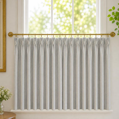 Close up of grey ticking stripe pinch pleats on a brass cafe rod with a garden view behind.