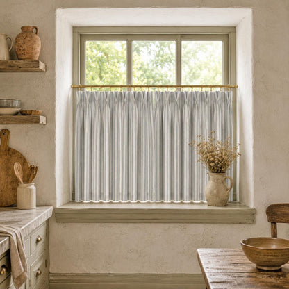 Ticking stripe kitchen tier curtain on a brass rod in a warm plaster kitchen with pottery shelf.