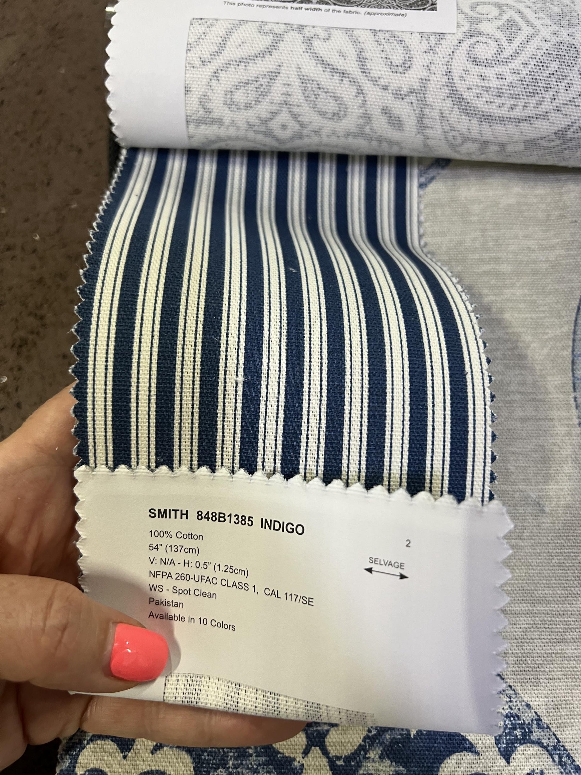 Hand holding an Alendel Smith indigo ticking stripe cotton swatch with the fabric label shown.