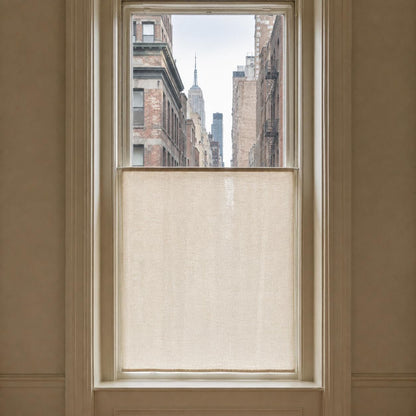 Tall city window with a flat sheer cafe curtain on the lower half, overlooking a New York street view