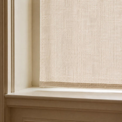 Detail of a flat sheer linen cafe curtain hem and weave against a deep windowsill in soft daylight
