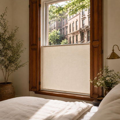 Close view of a bedroom window with a flat sheer cafe curtain, brass wall sconce and historic brownstone view