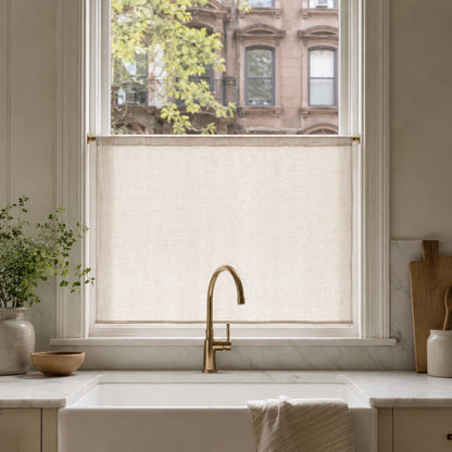 Beige faux linen cafe curtain covering the lower half of a kitchen window above a farmhouse sink