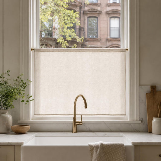 Beige faux linen cafe curtain covering the lower half of a kitchen window above a farmhouse sink