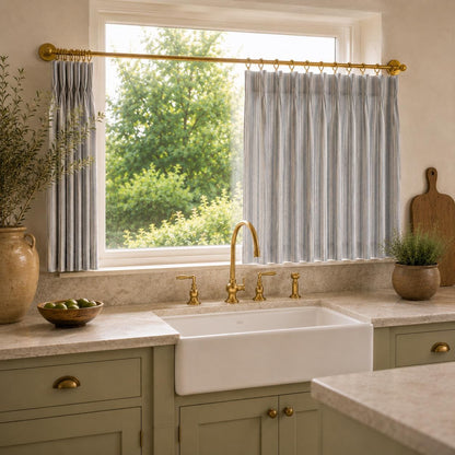 Ticking stripe cafe curtain over a kitchen sink with brass tap, marble counter and wood board.