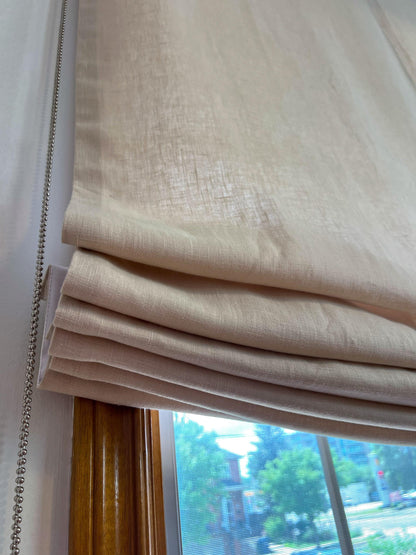 Close-up of relaxed Roman shade folds in natural linen with silver bead chain on a wooden window frame