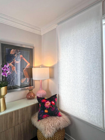 White linen relaxed Roman shade lowered, filtering daylight in a bedroom reading corner