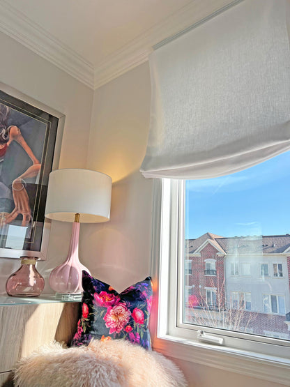 White linen relaxed Roman shade raised with a soft curved fold above a sunny window