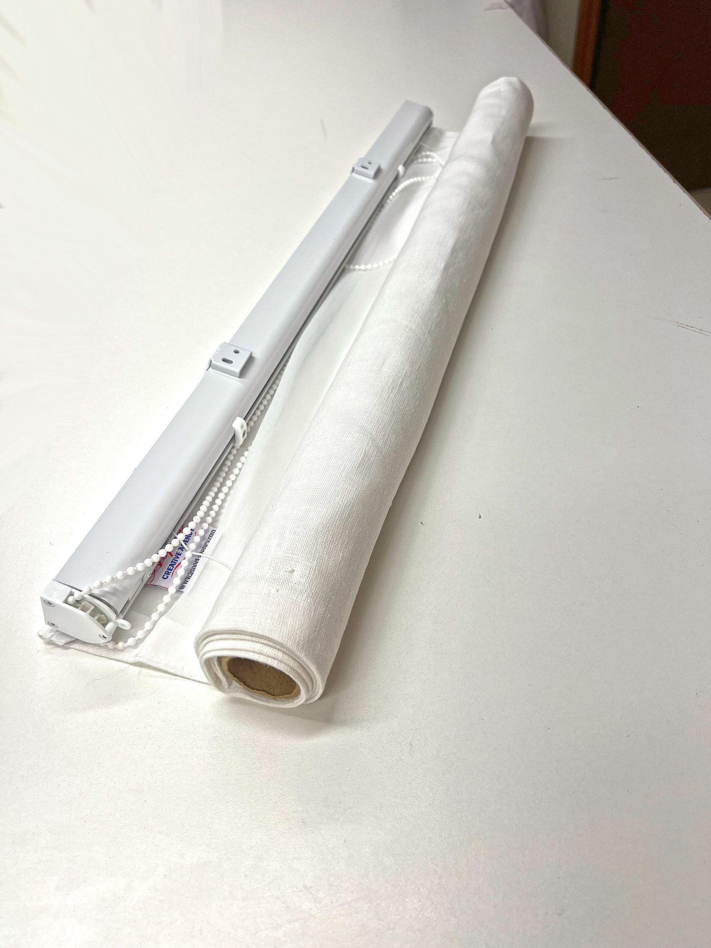 What arrives in the box: aluminium headrail with chain and the rolled linen Roman shade, ready to install
