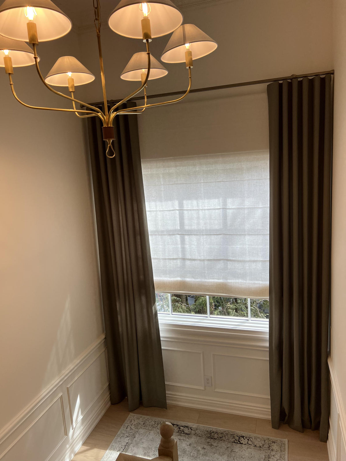 Linen Roman shade layered with dark floor length drapery under a chandelier