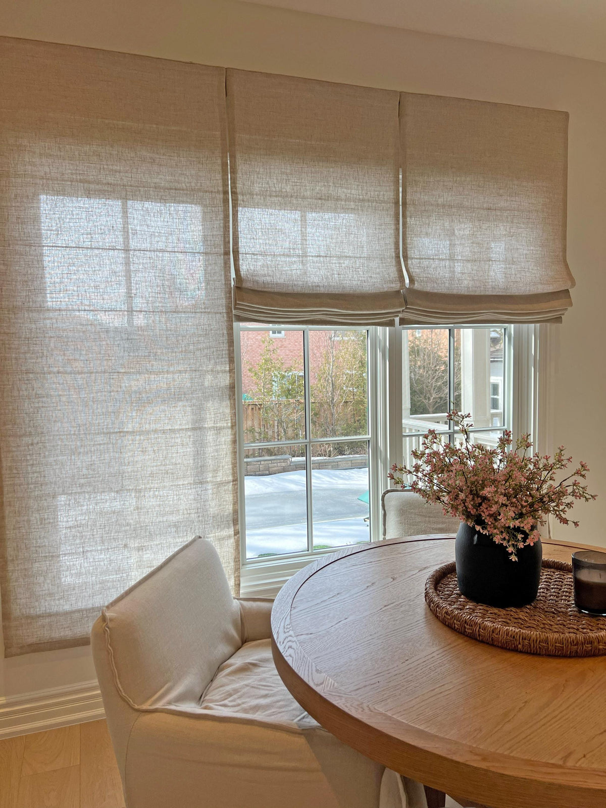 Linen Roman shades in a dining bay window above a round table with dried flowers