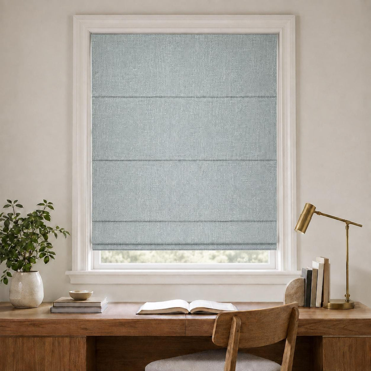 Soft blue grey linen Roman shade above a wooden desk in a home office