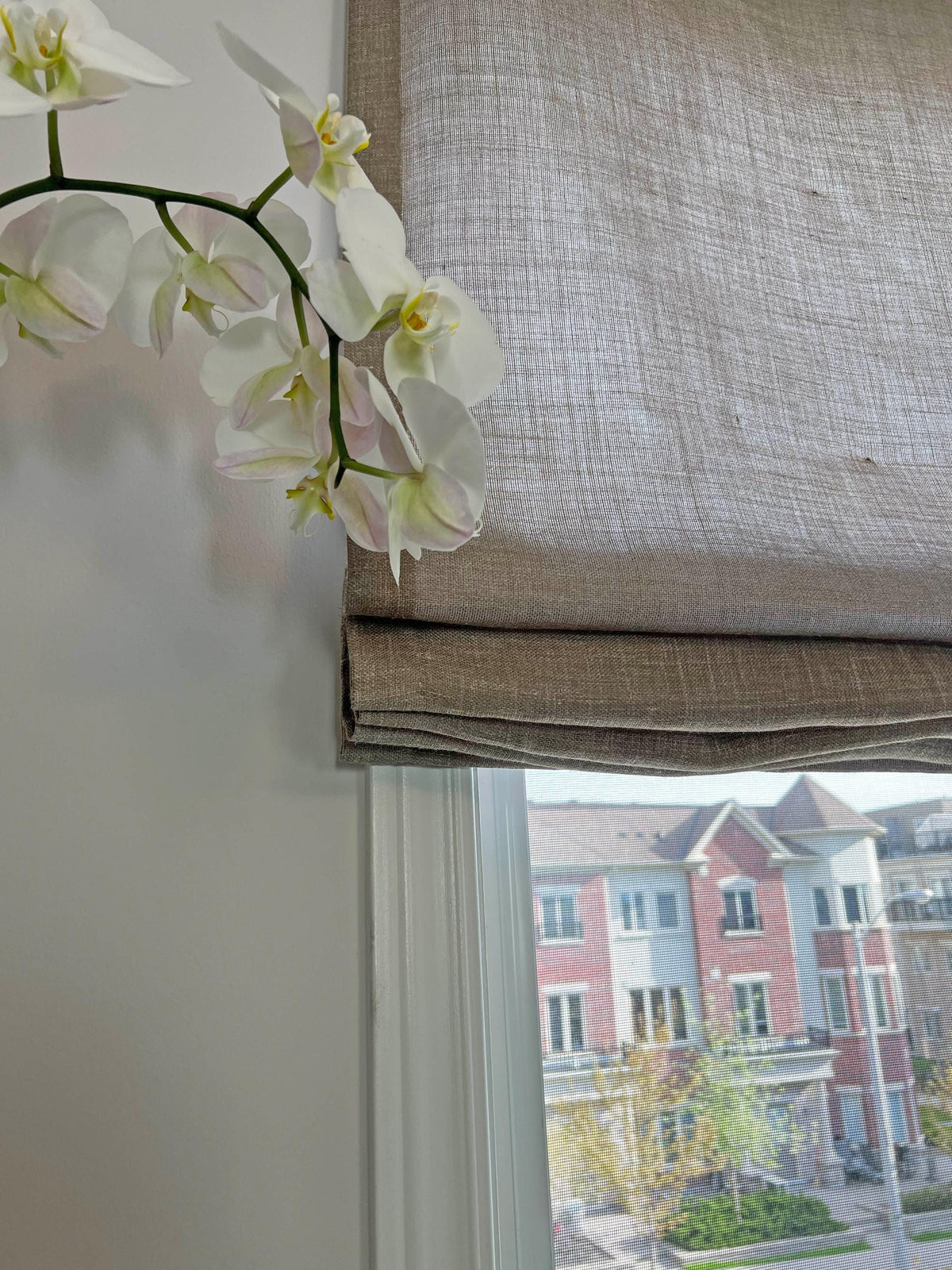 Textured linen Roman shade with an orchid on the sill, daylight through the weave