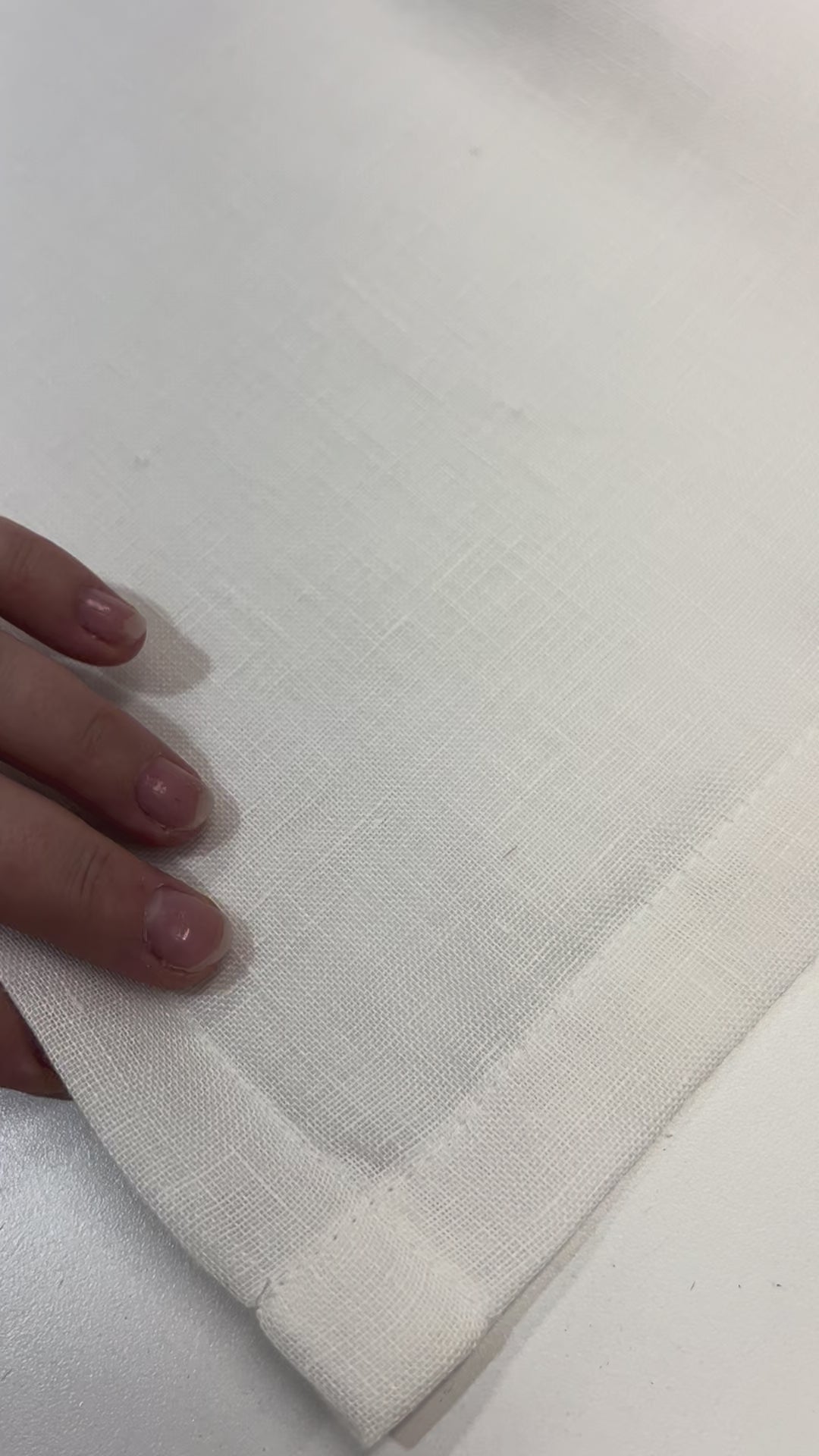 Video: hands showing the double-folded hem and clean corner stitching of a sheer linen cafe curtain