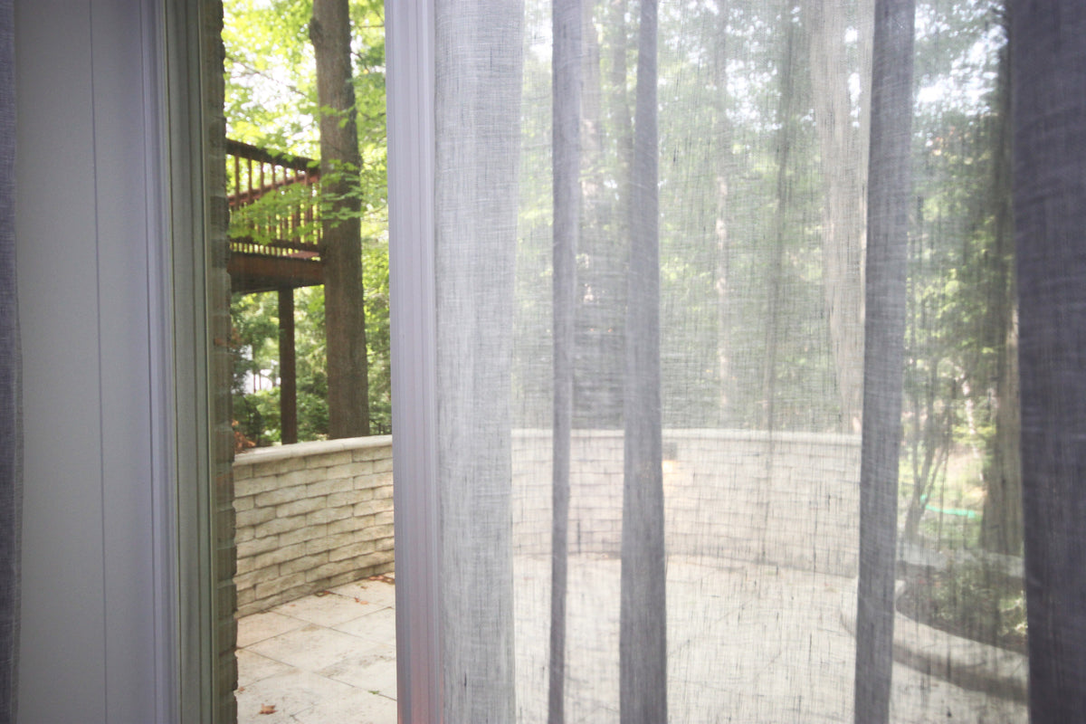 Grey Brent linen-blend sheer ripple fold curtains filtering a wooded view onto a stone patio