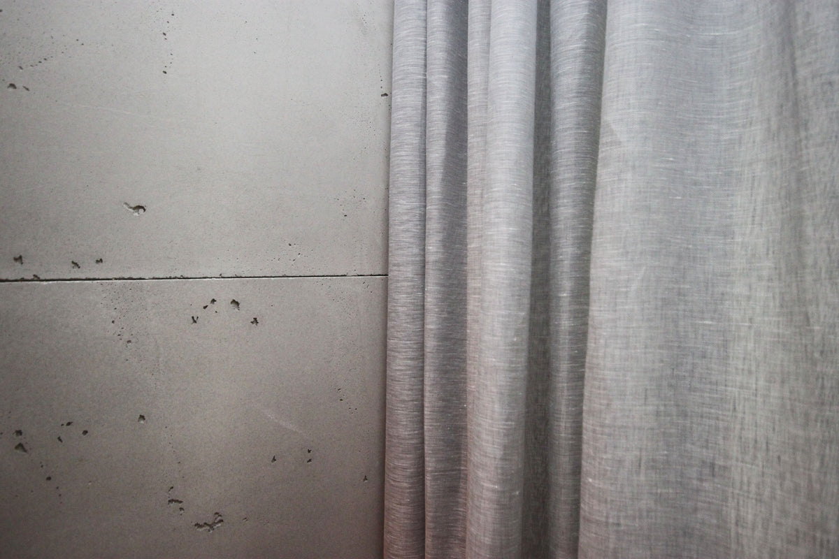 Edge of a grey Brent sheer ripple fold panel against a concrete wall, showing the light linen weave
