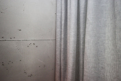 Edge of a grey Brent sheer ripple fold panel against a concrete wall, showing the light linen weave