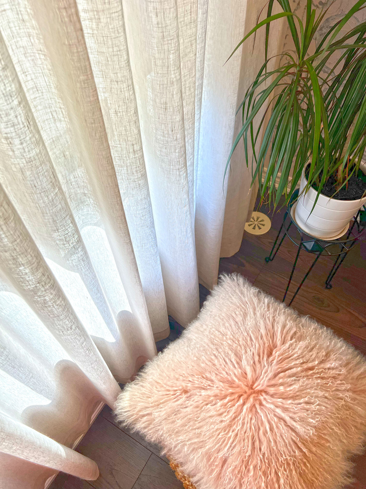 Hem of a Brent Candle sheer ripple fold panel just above a wood floor, beside a plant and a pink fur pouf